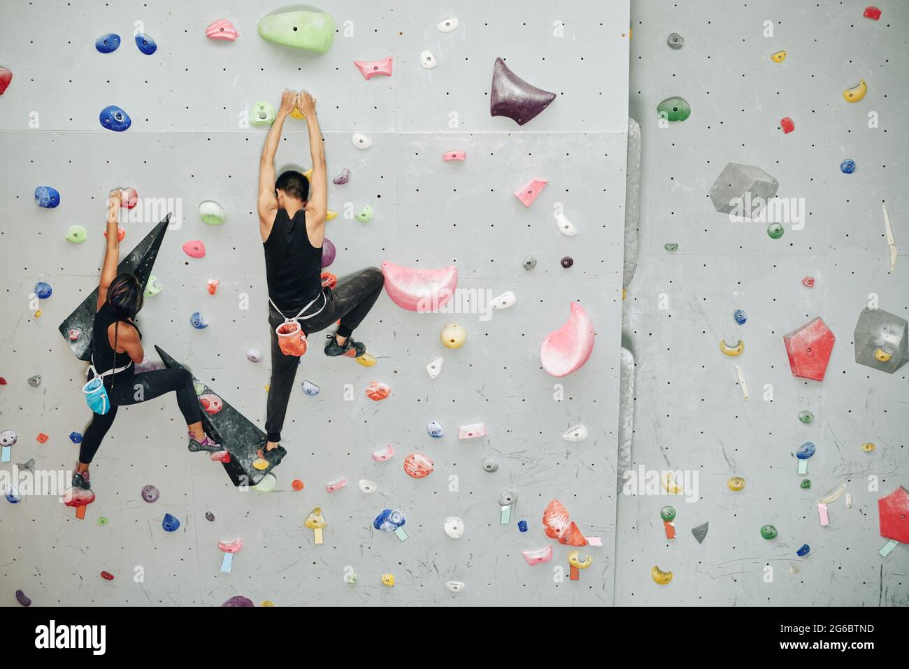Young couple climbing up the wall when training for competition at