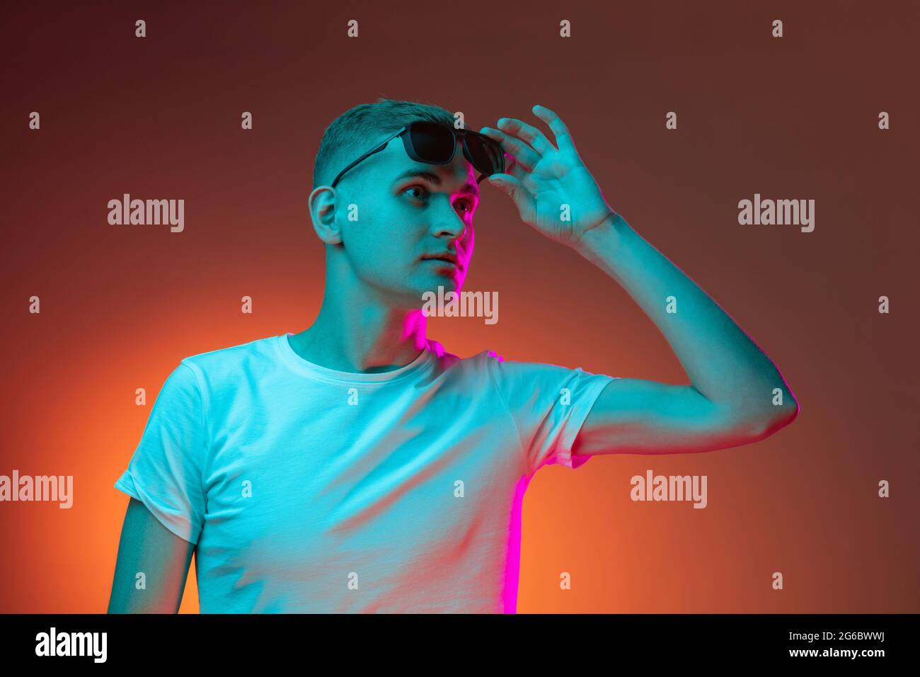 Portrait of young Caucasian man in casual clothes isolated over gradient red orange studio background in neon light with copyspace for ad. Concept of Stock Photo