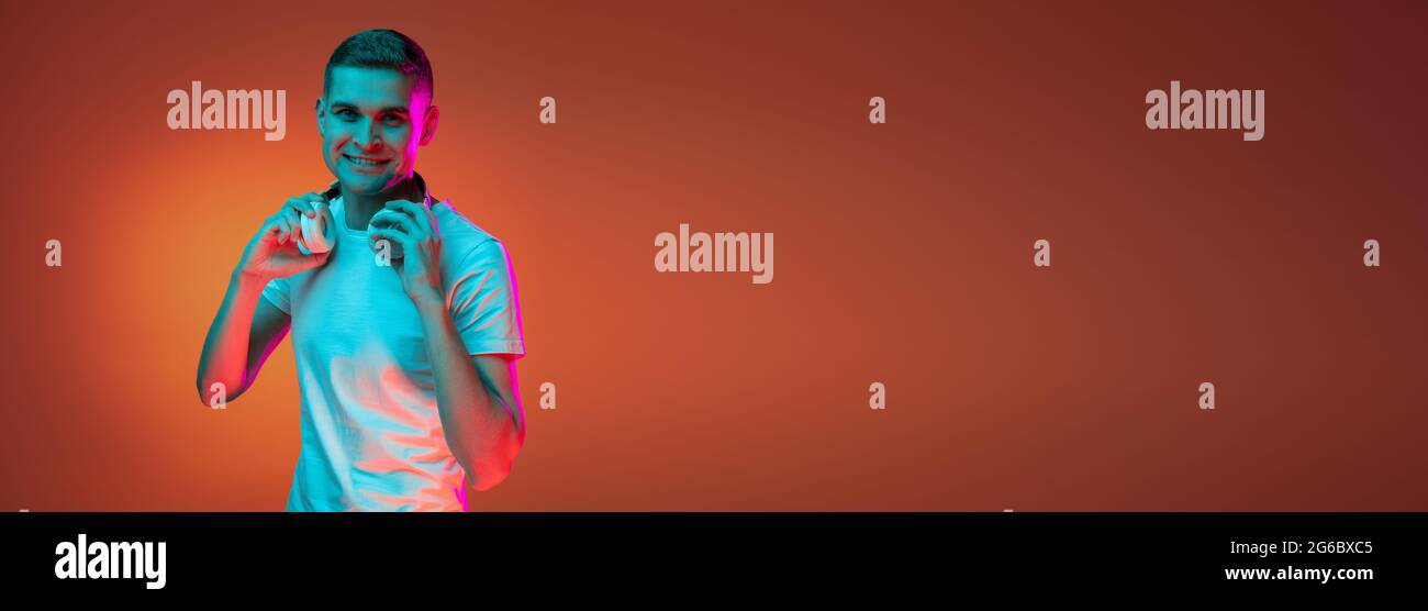 Portrait of young Caucasian man in casual clothes isolated over gradient red orange studio background in neon light with copyspace for ad. Concept of Stock Photo