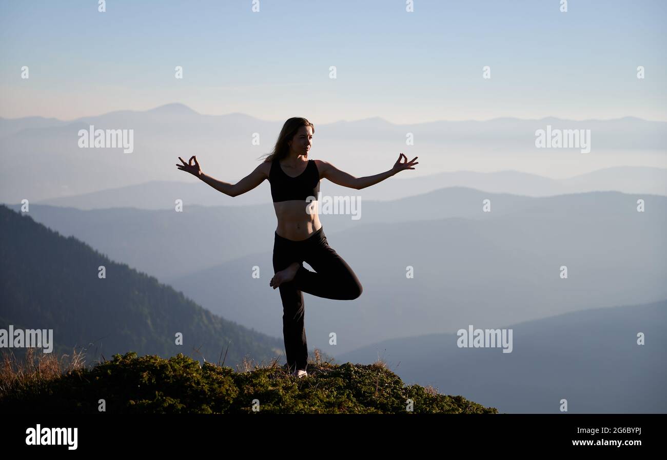 Woman practicing yoga balancing on one leg on a mat in a high key