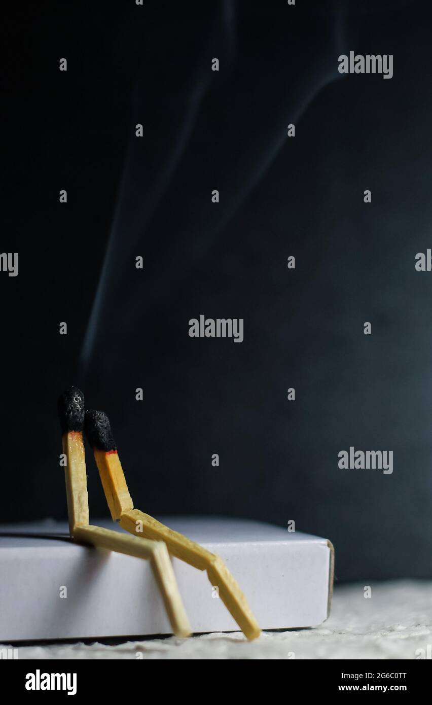 Two matches burning sitting together on the matchbox in the dark copy space. Two matches in