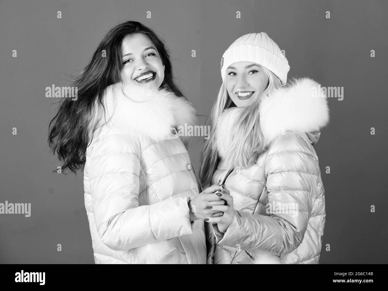 Fashion friends. Winter clothes. Women wear down jacket with furry hood. Girls smiling makeup faces wear jackets blue background. Winter season Stock Photo
