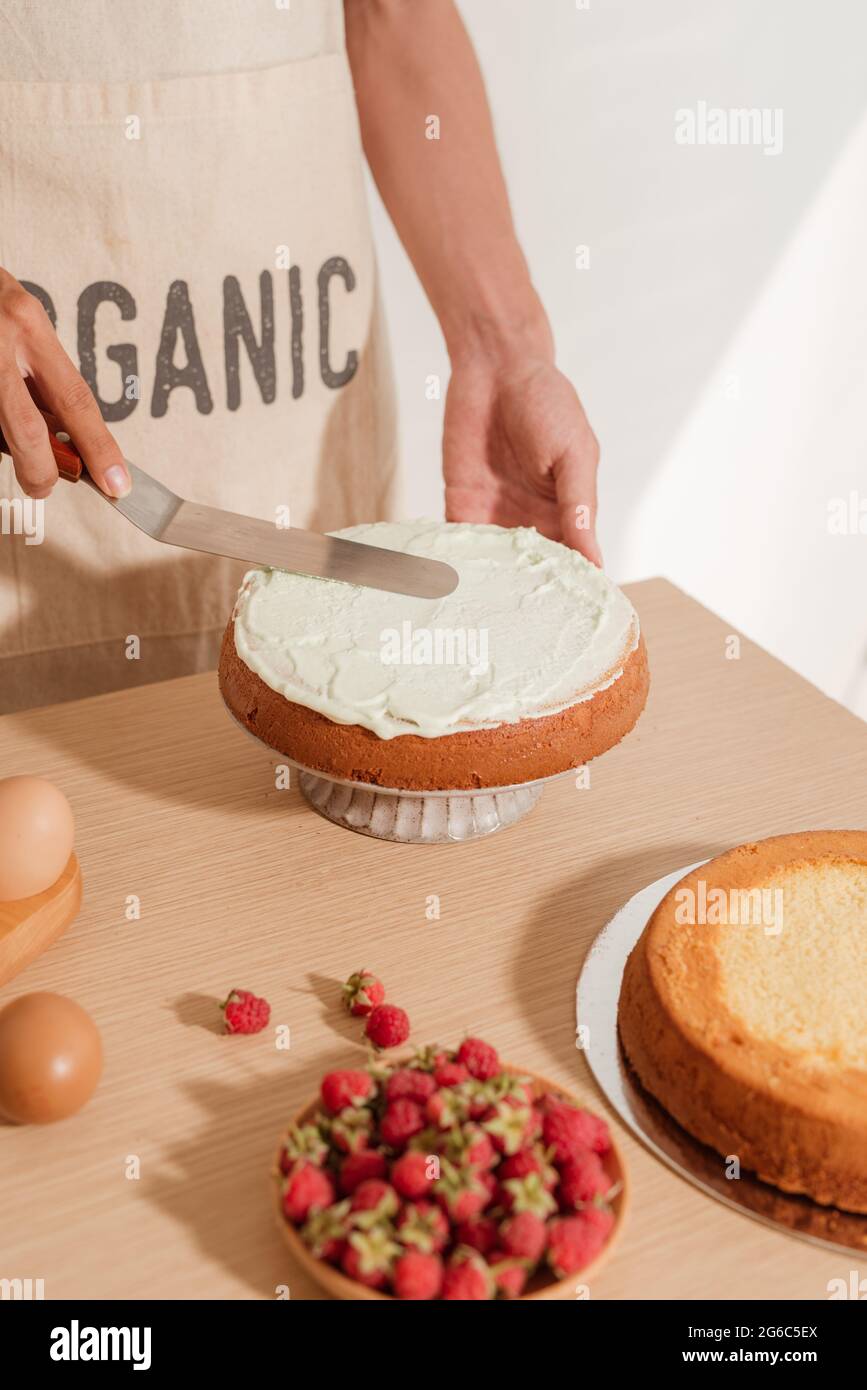 Man pastry chef put icing cream on sponge cake. Making sponge cake series Stock Photo