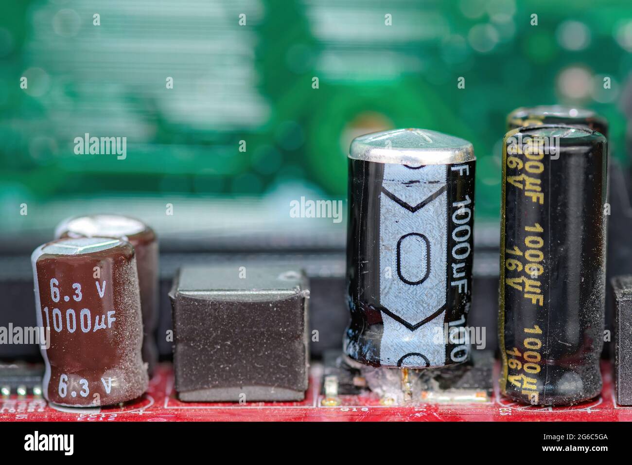 Damaged capacitor on a circuit board. Top is bulged out showing failure. Undamaged capacitors also present. No brand markings. Shallow depth of field. Stock Photo