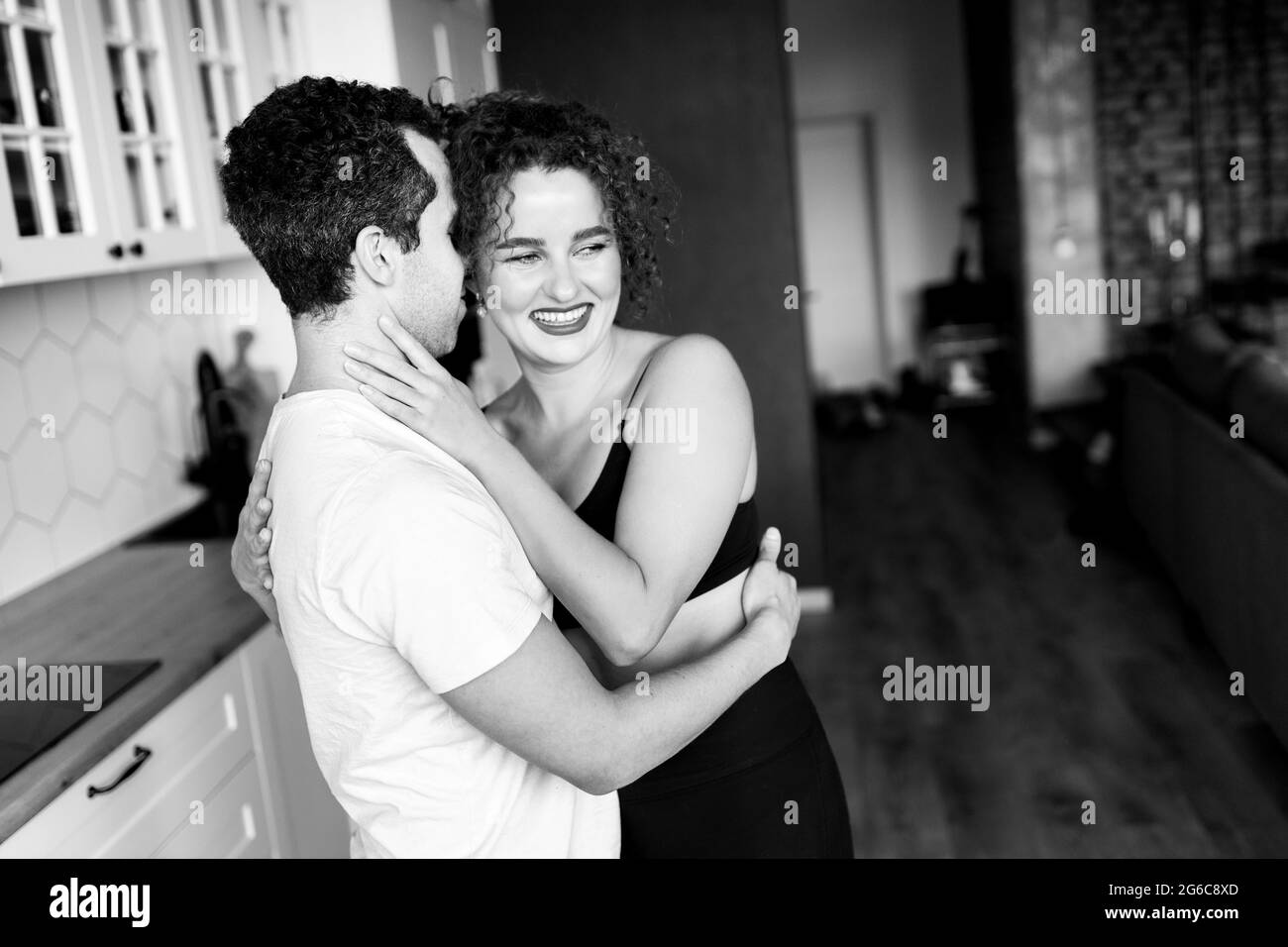 Black and white portrait of Caucasian loving young lady looking at camera and embracing hugging her lover or husband with tenderness. Happy beloved Stock Photo