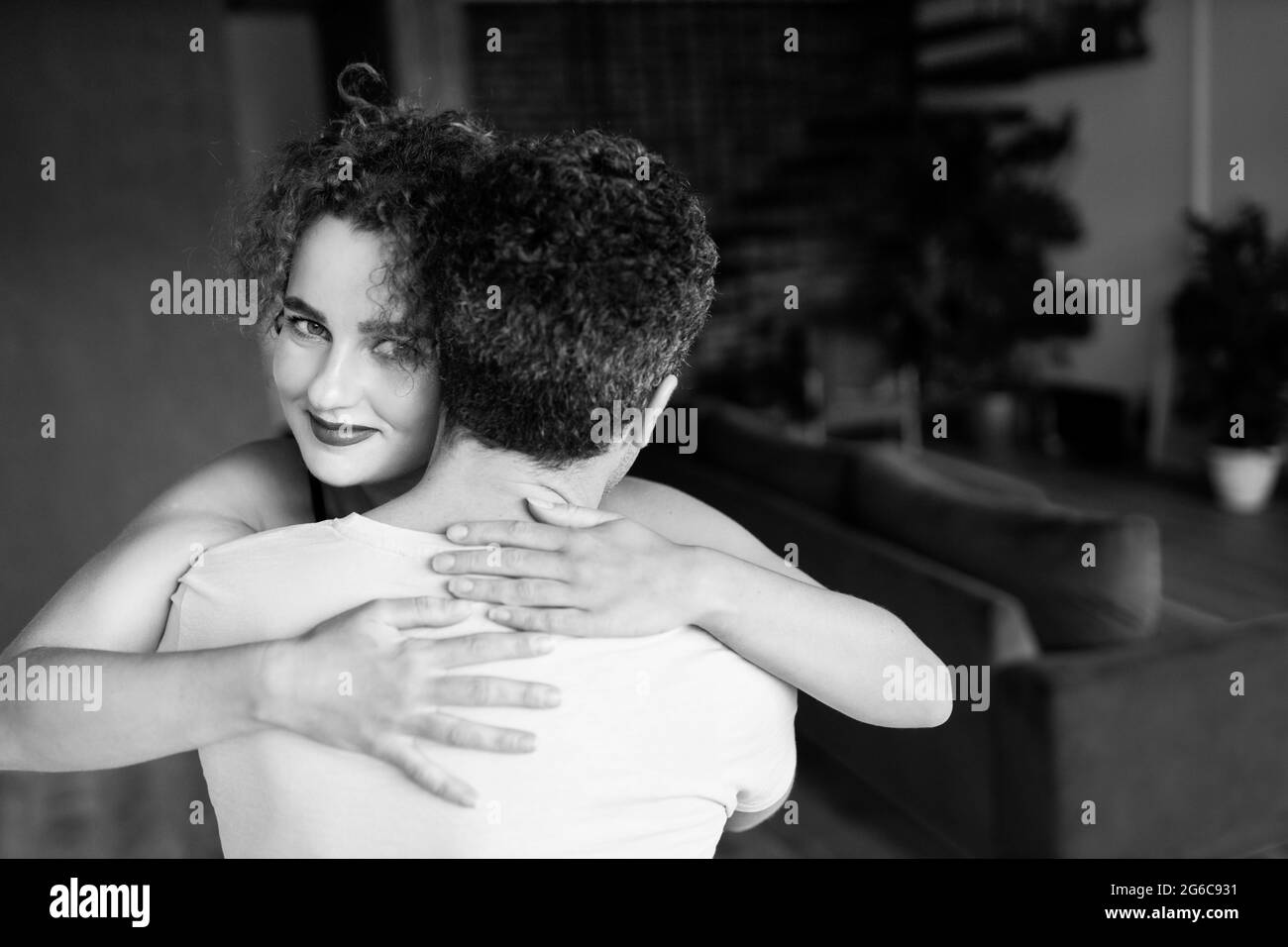 Black and white portrait of Caucasian loving young lady looking at camera and embracing hugging her lover or husband with tenderness. Happy beloved Stock Photo