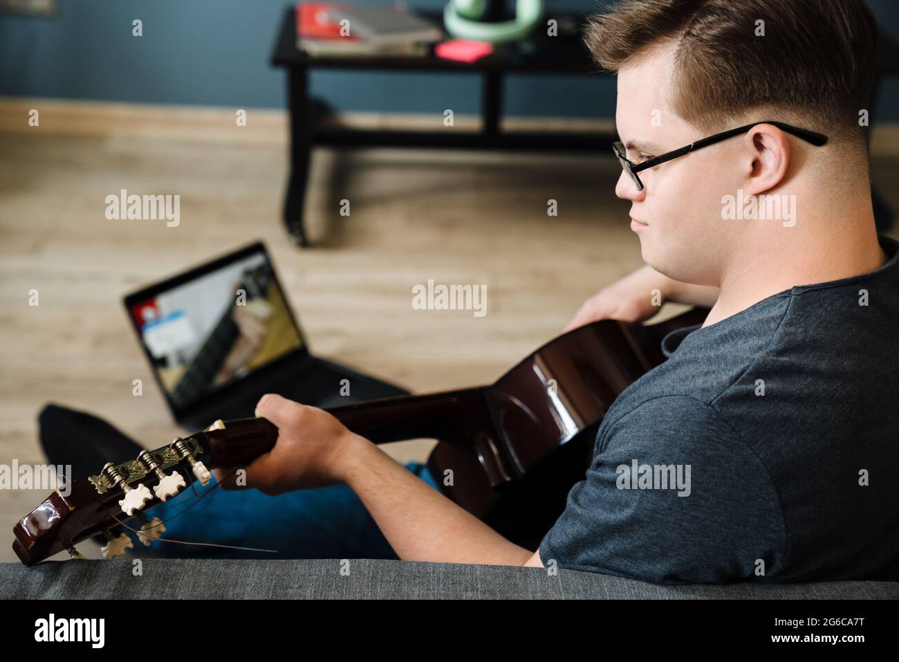 Young man with down syndrome playing guitar while using laptop at home Stock Photo