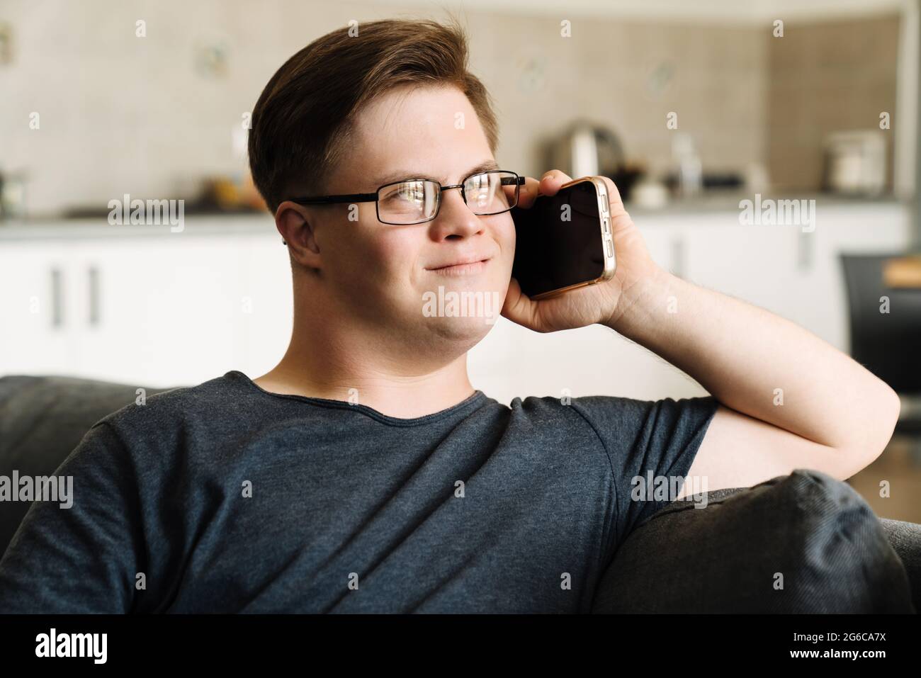 Young man with down syndrome talking on cellphone while sitting at home Stock Photo