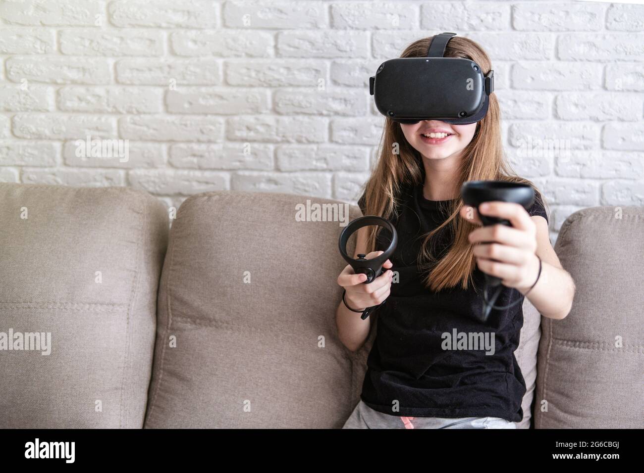 Girl wearing virtual reality VR simulator playing with joysticks at home. High quality photo Stock Photo