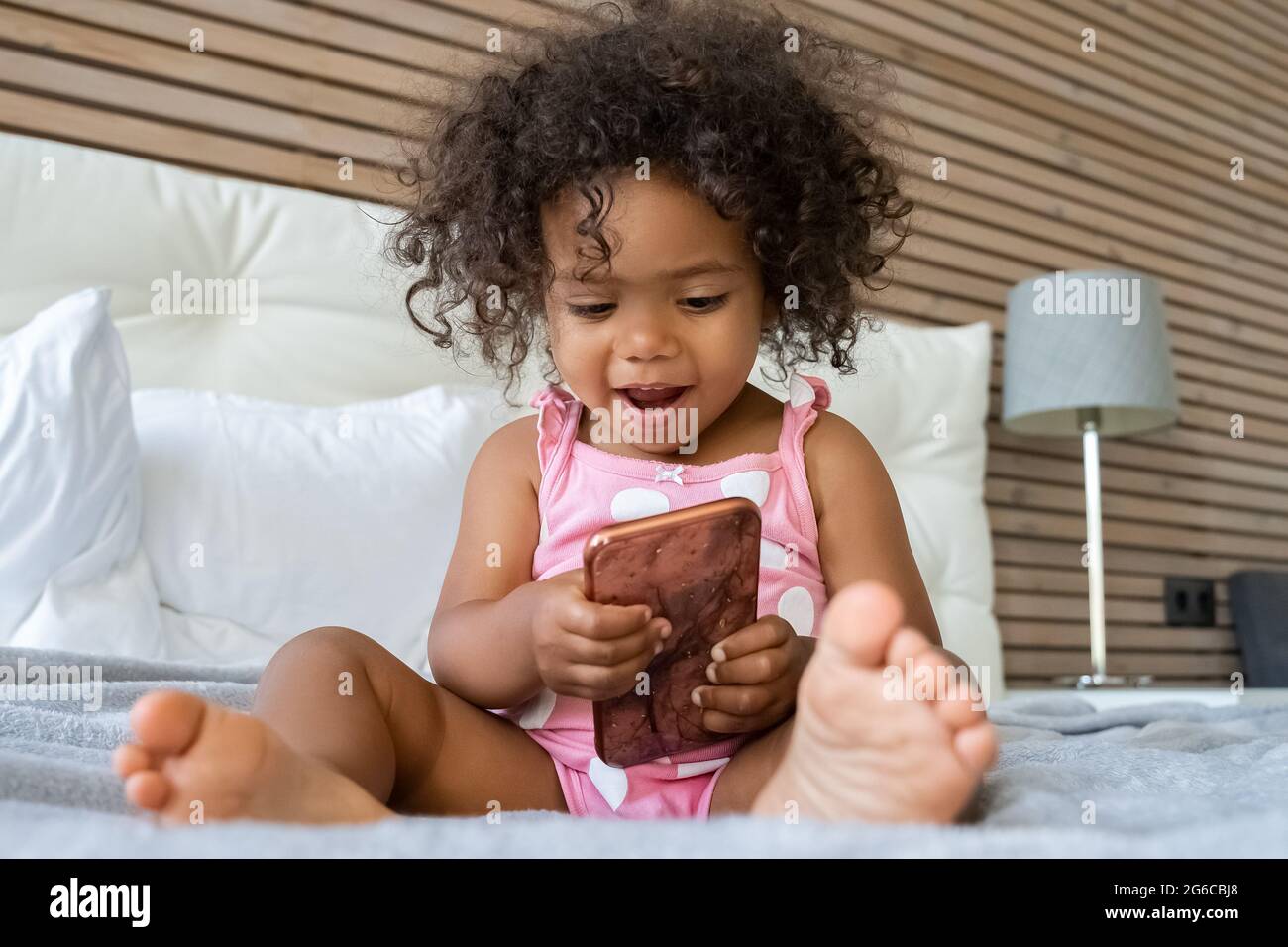 Surprised smiling girl child using smart phone sitting on bed in bedroom Stock Photo