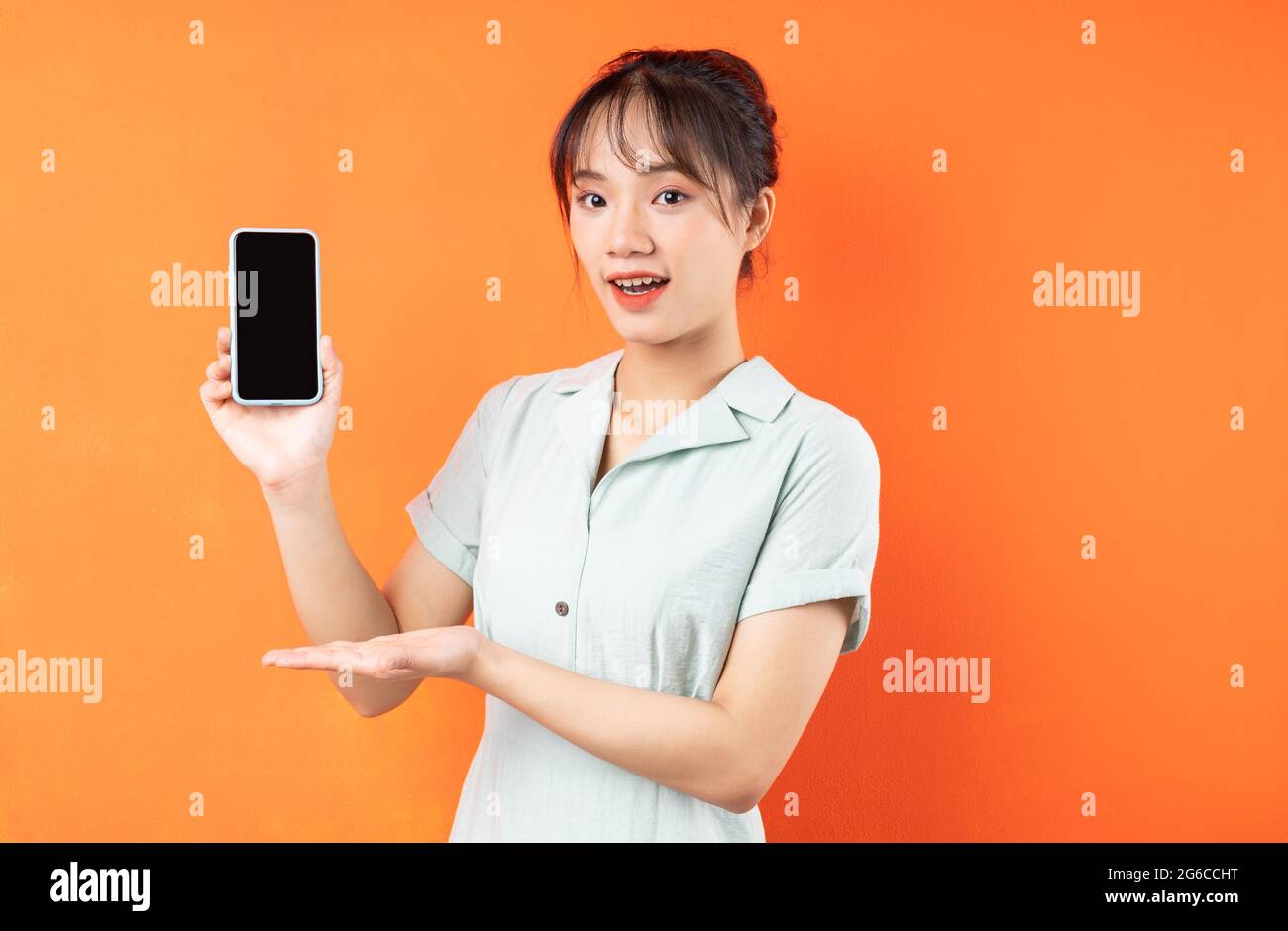 Portrait of young girl showing phone screen, isolated on orange background Stock Photo