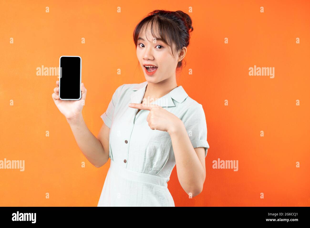 Portrait of young girl showing phone screen, isolated on orange background Stock Photo