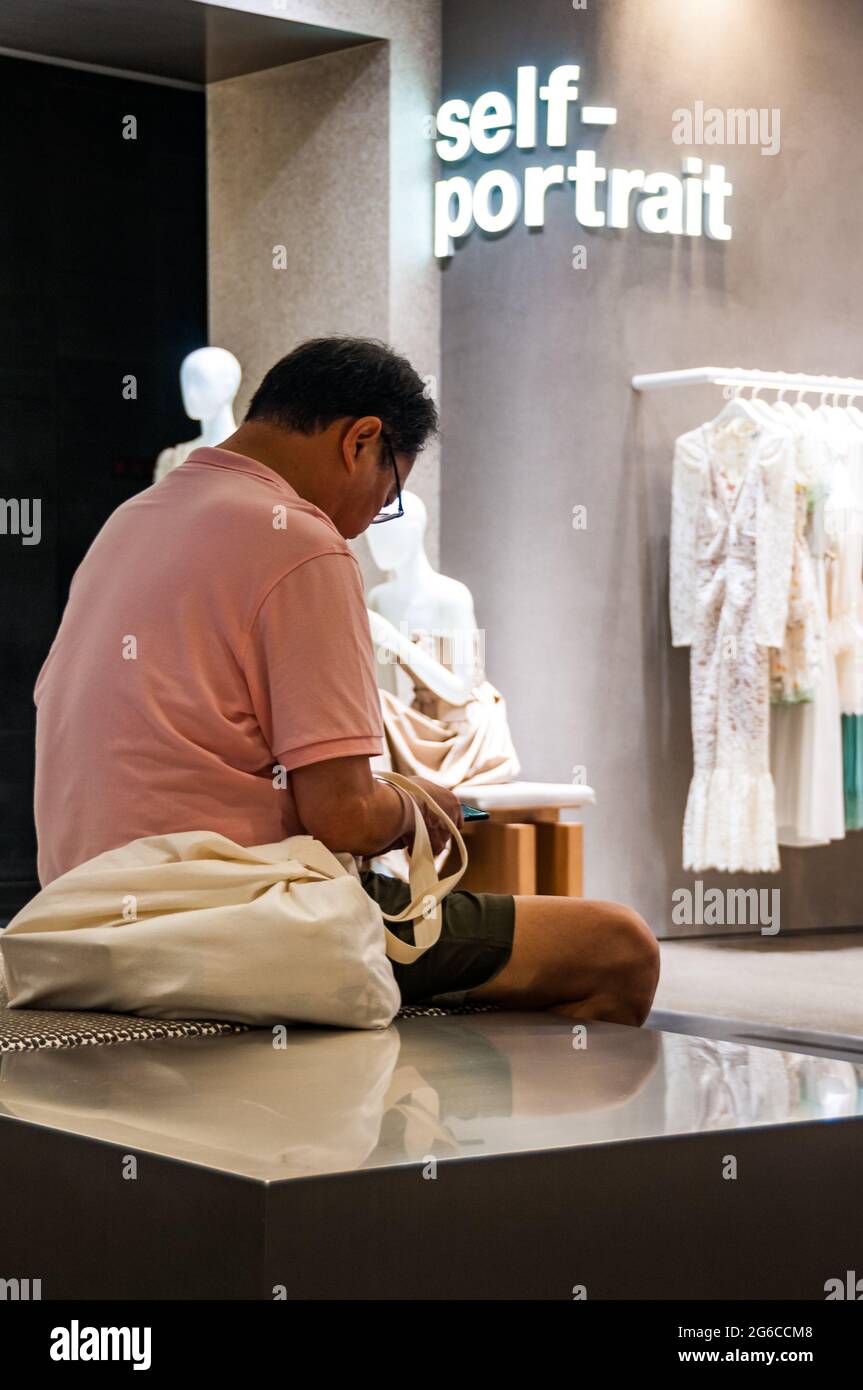 A man sitting in the Reel shopping mall in front of a sign saying self-portrait at Jing’an Temple, Shanghai, China. Stock Photo