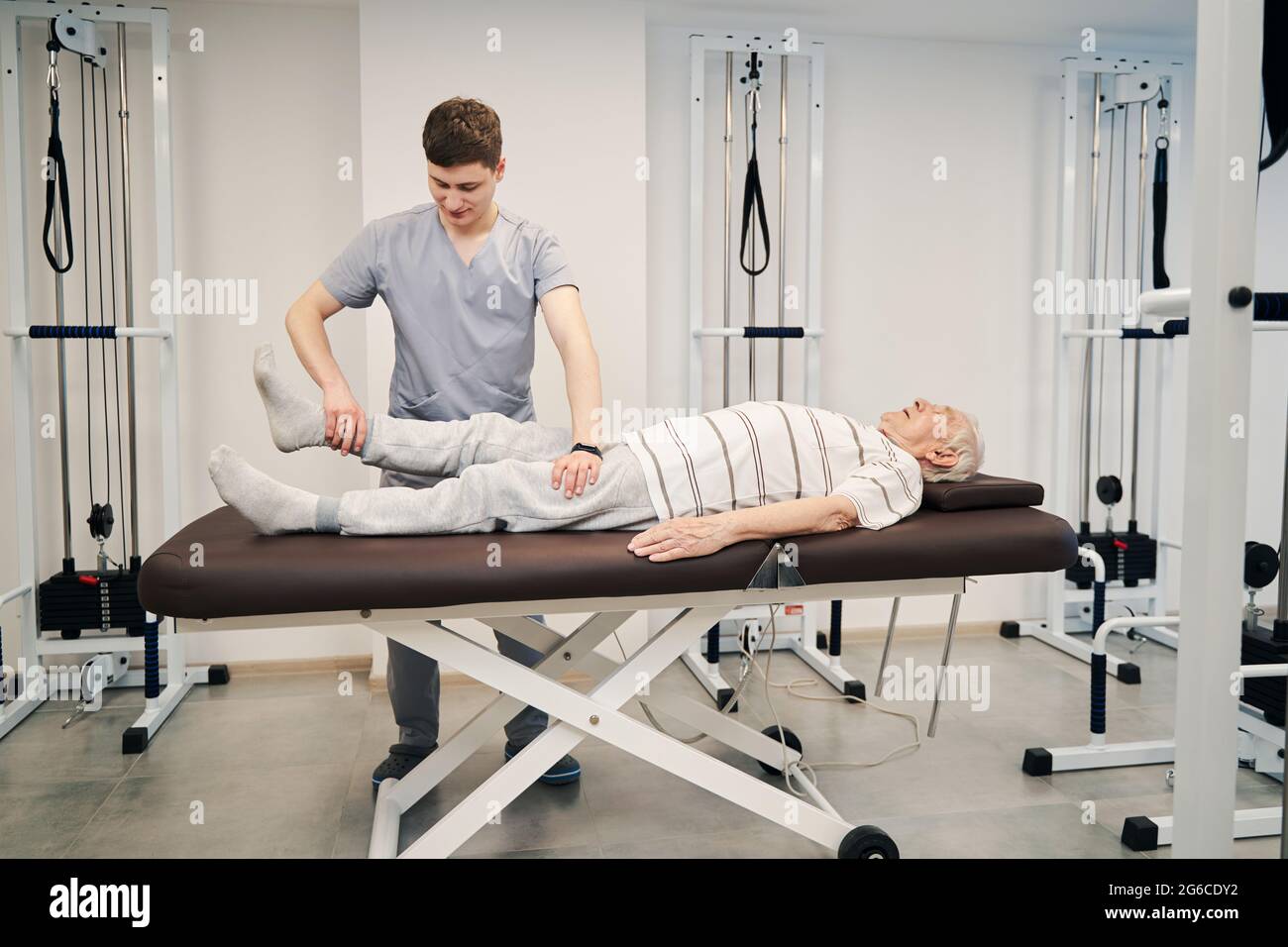 Physical therapist pulling old male right leg during treatment activity