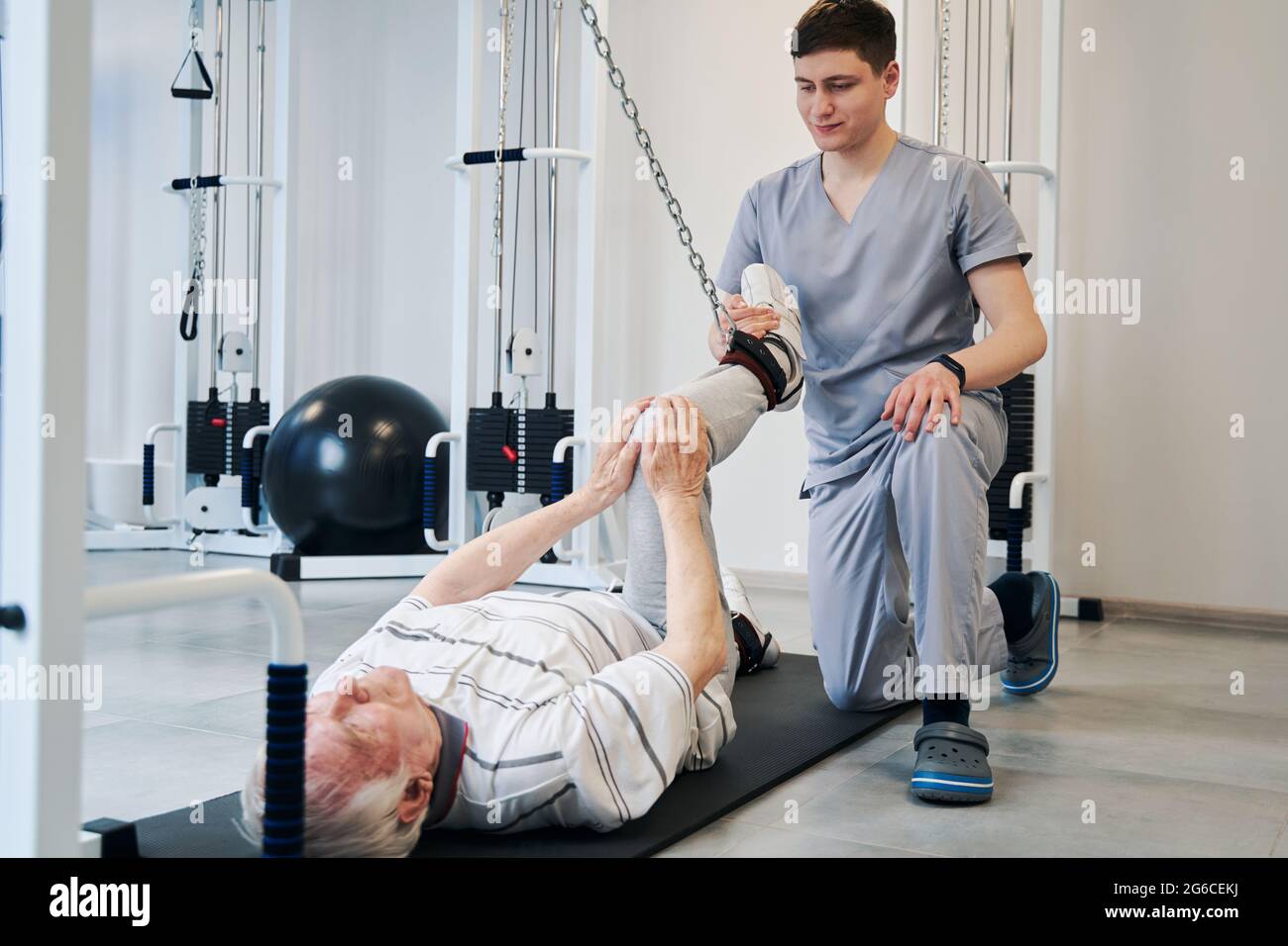 Doctor pulling right leg of pensioner with attached resistance band