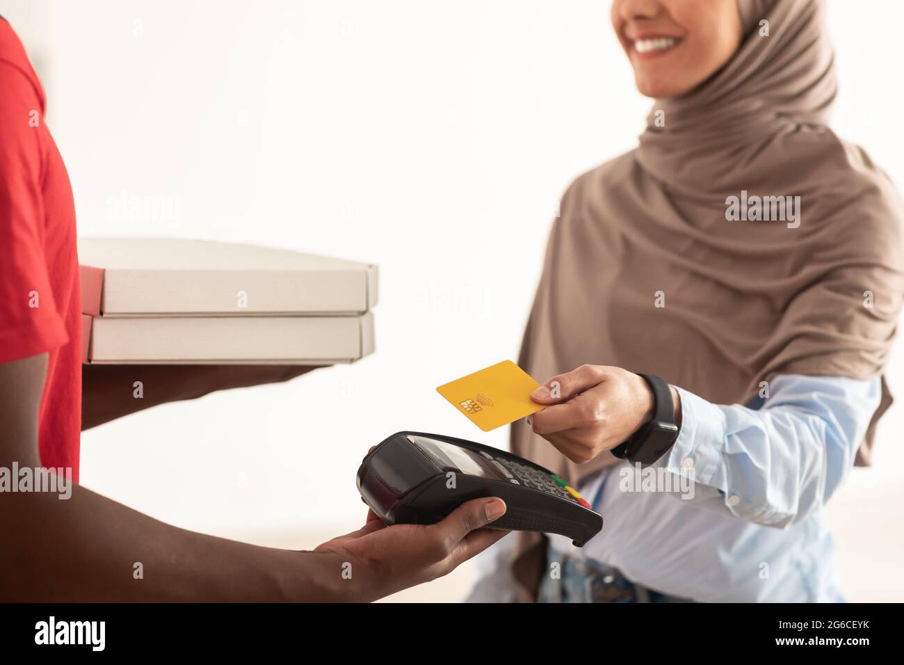 Deliveryman holding POS machine, muslim client paying with card Stock Photo