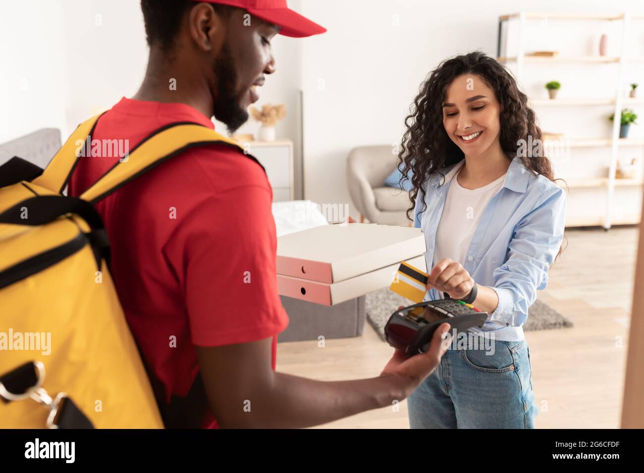 Smiling deliveryman holding POS machine, woman paying with card Stock Photo