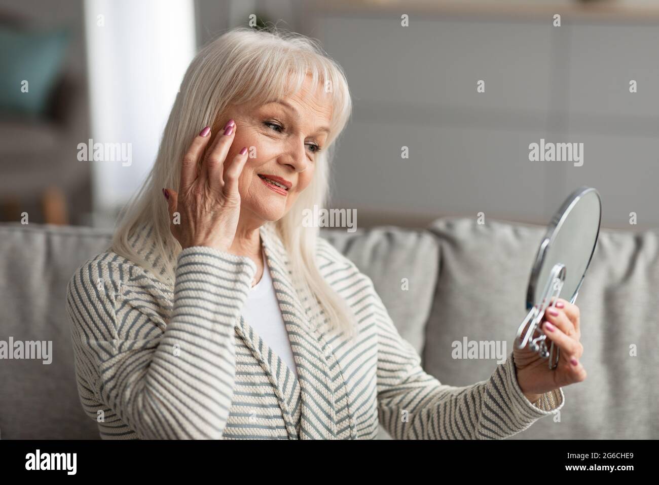 Smiling adult woman checking her face looking in mirror Stock Photo