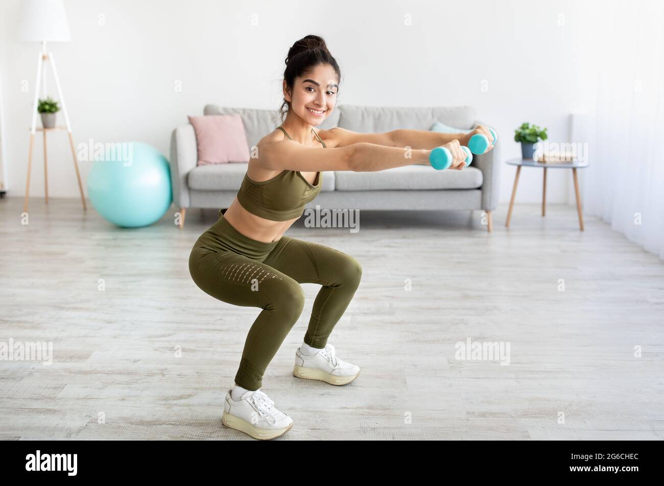 Strong young Indian woman working out with dumbbells, squatting at home, empty space Stock Photo