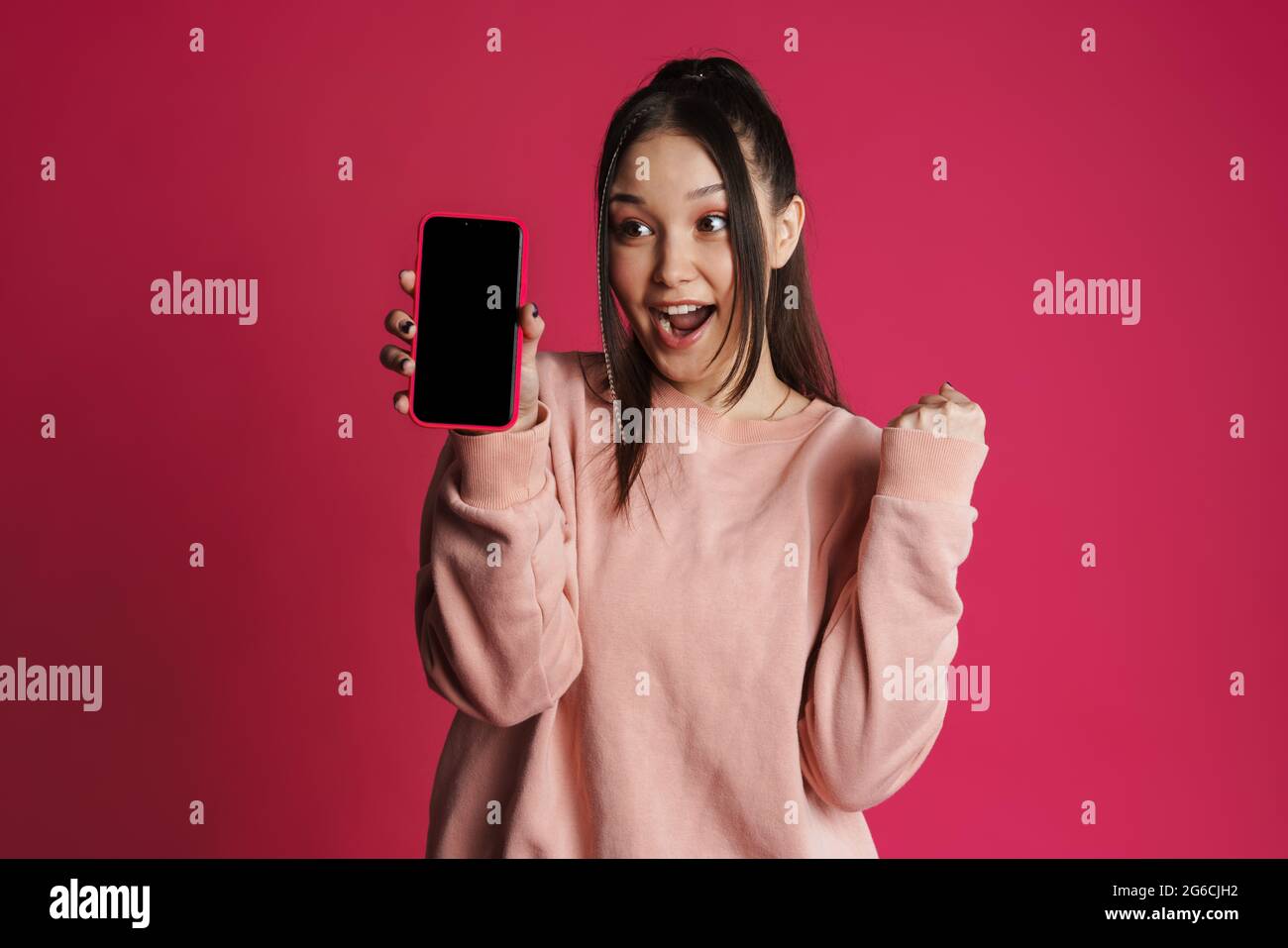 Asian excited woman showing winner gesture and cellphone isolated over ...