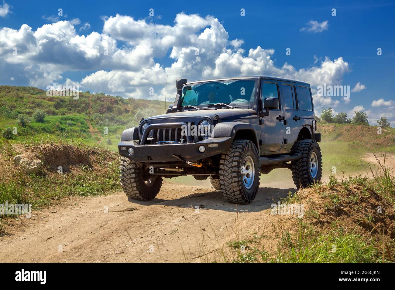black SUV car with a winch and big wheels for off-road driving travels along a rough trail on clay hilly landscapes with slopes on a sunny day with cl Stock Photo