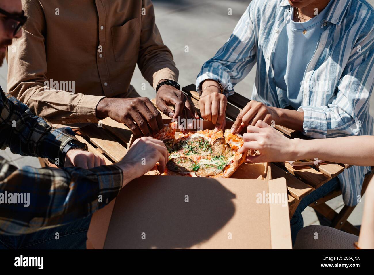 Close up of group of young people enjoying pizza outdoors, scene lit by sunlight, copy space Stock Photo