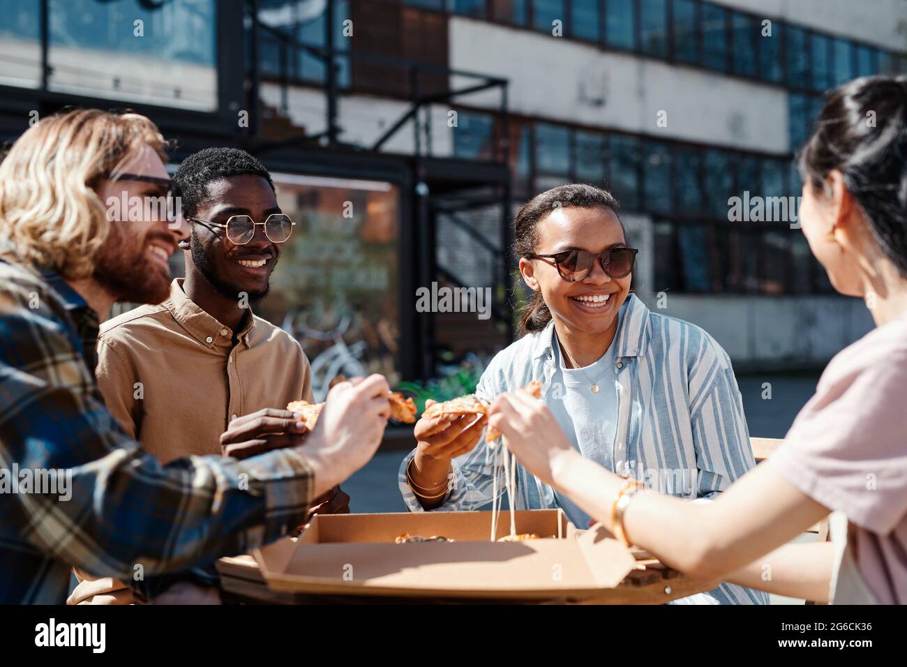 Diverse group of contemporary young people enjoying pizza outdoors, scene lit by sunlight, copy space Stock Photo