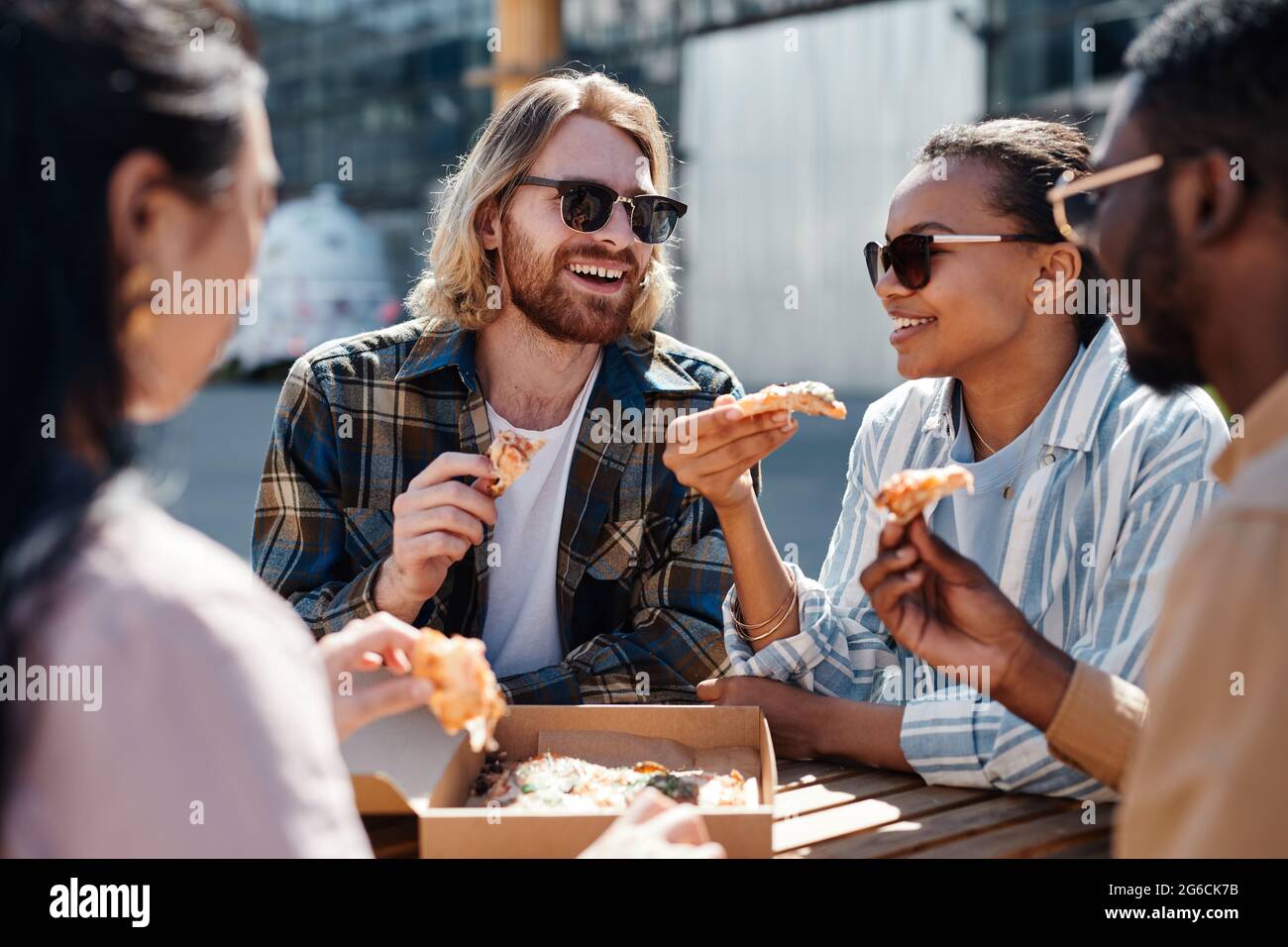 Diverse group of carefree young people enjoying pizza outdoors, scene lit by sunlight, copy space Stock Photo