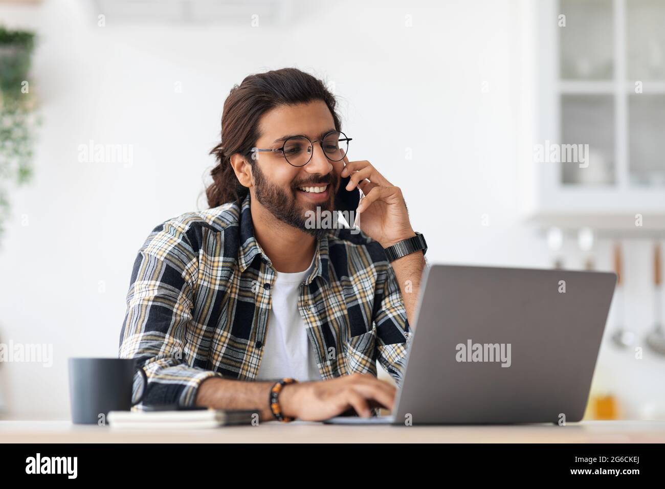 Smiling arab man freelancer talking on phone and taking notes Stock Photo