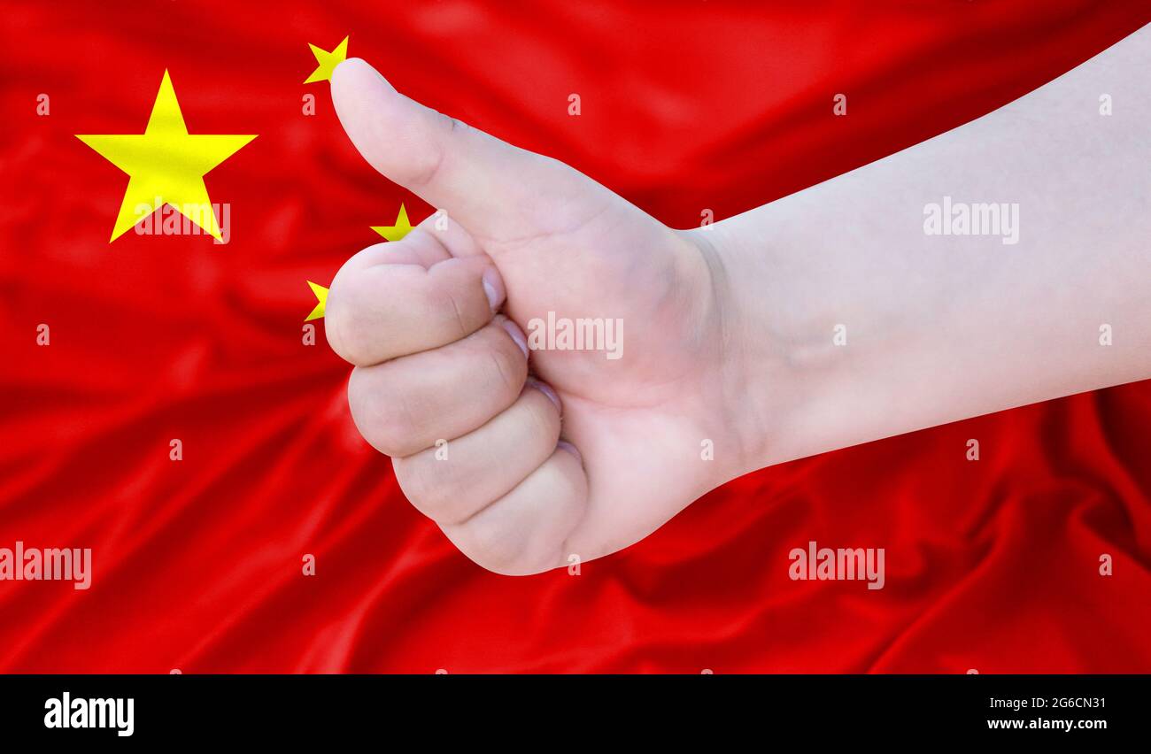 Hand makes a thumbs up sign on the background of the flag of China. like, good, positive Stock Photo