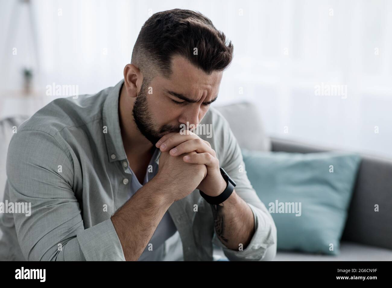 Unhappy depressed caucasian handsome bearded man crying in living room couch, feeling desperate Stock Photo