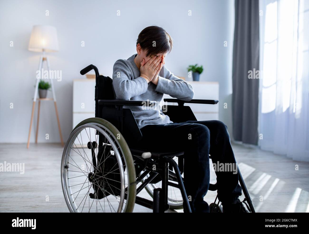 Depression in disabled teenagers. Unhappy handicapped teen boy in wheelchair crying at home Stock Photo