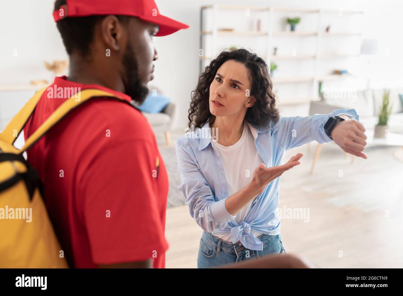 Frustrated female customer pointing at watch, delivery man is late Stock Photo