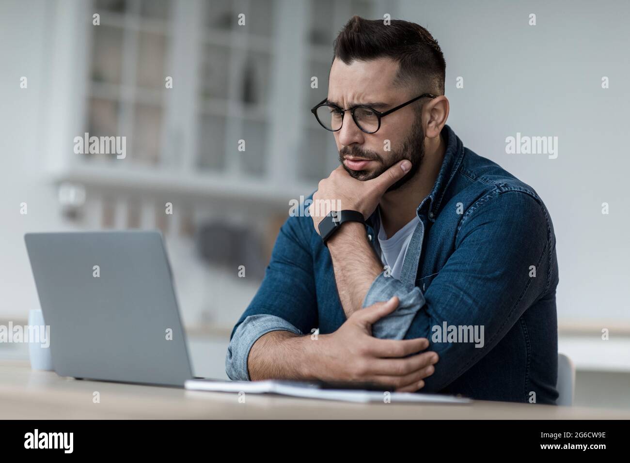 Thoughtful businessman think of online project, look at laptop at workplace, professional consider solution Stock Photo