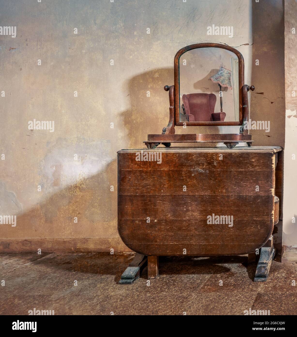 Mirror on old table reflecting chair, lamp. Vintage, retro furniture items in abandoned old derelict house. Stock Photo