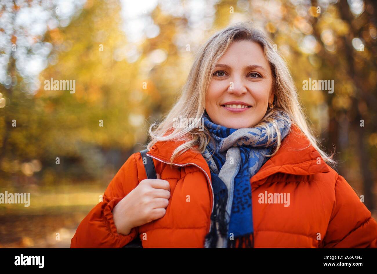 Delighted female in outerwear smiling on sunny weekend day in autumn park Stock Photo