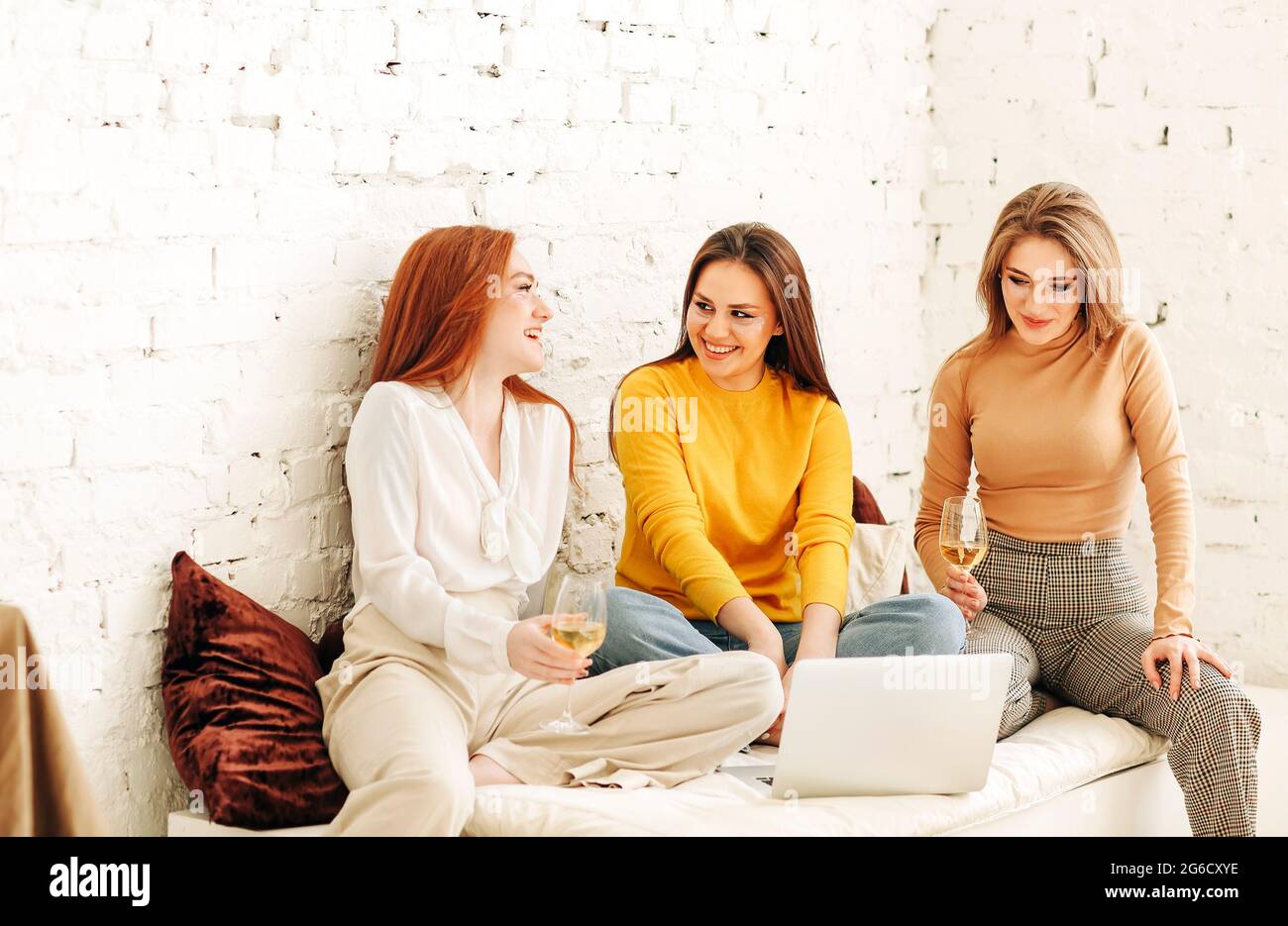 Optimistic young women smiling with eye patches on face while resting near rough brick wall watching movie on computer Stock Photo
