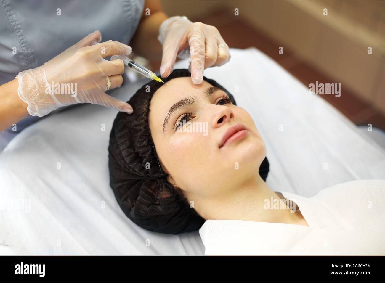 Professional beautician injecting hyaluronic acid near eyes of woman