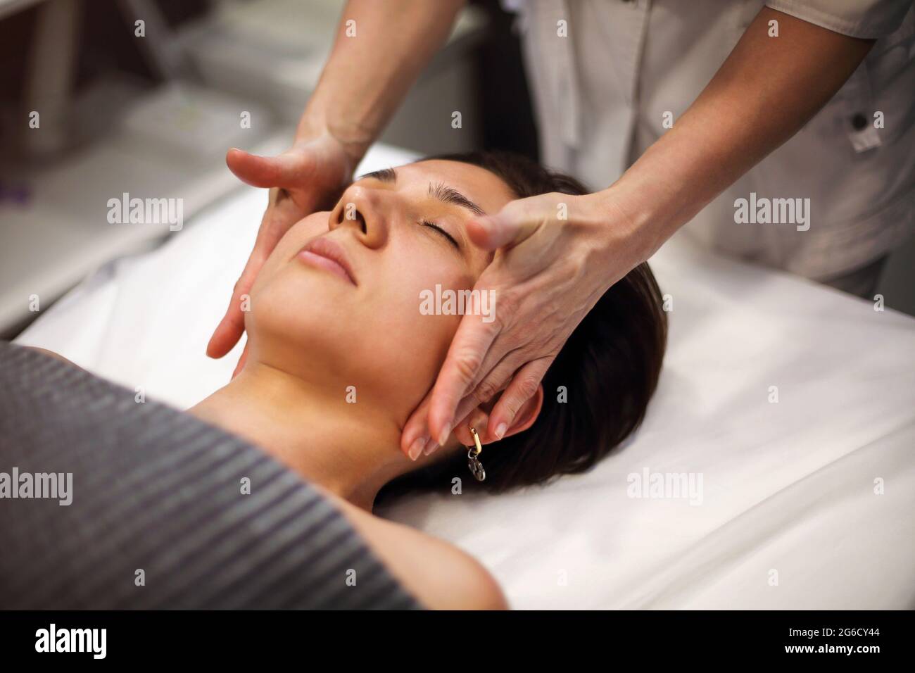 Unrecognizable masseuse in gown standing in spa salon and massaging face of female customer Stock Photo