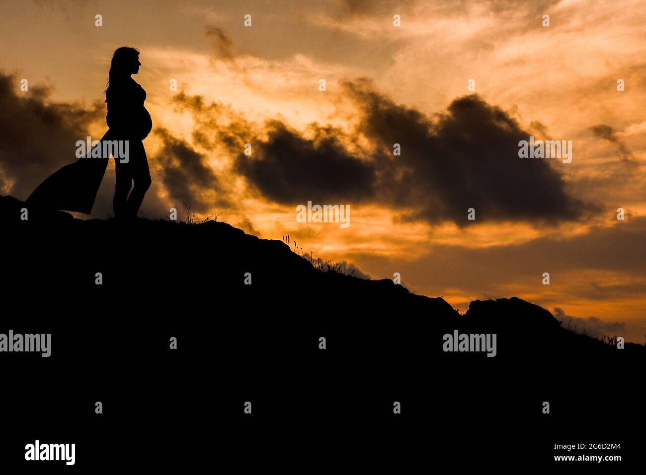 Low angle side view silhouette of anonymous pregnant female standing alone on hill and dreaming about future at sunset time Stock Photo