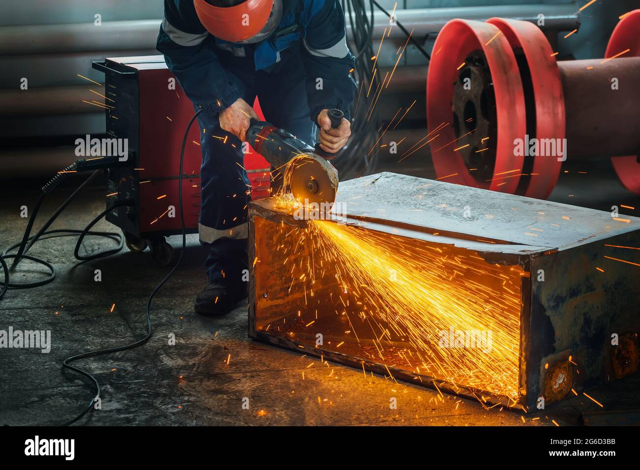 A worker cuts metal with a hand grinder in the production shop and bright sparks fly. A genuine working environment. A man at work. Stock Photo