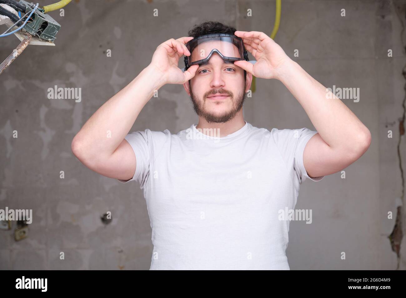 Young builder putting on safety glasses at a construction site. Man wearing  protective goggles Stock Photo - Alamy