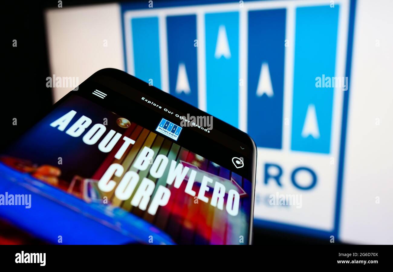 Mobile phone with website of American bowling center company Bowlero Corporation on screen in front of logo. Focus on top-left of phone display. Stock Photo