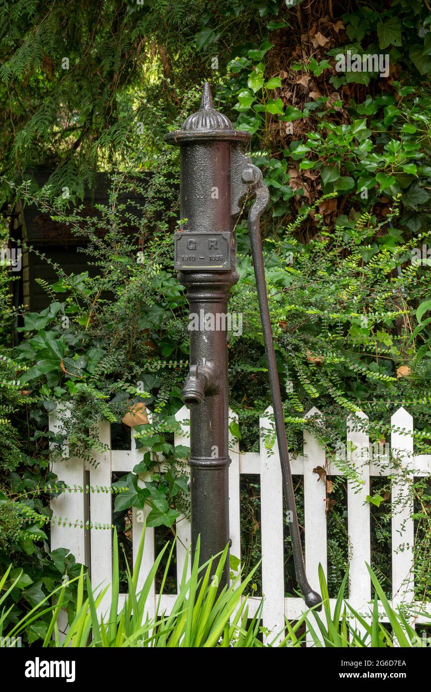 A vintage cast iron village hand water pump against trees and a picket fence Stock Photo