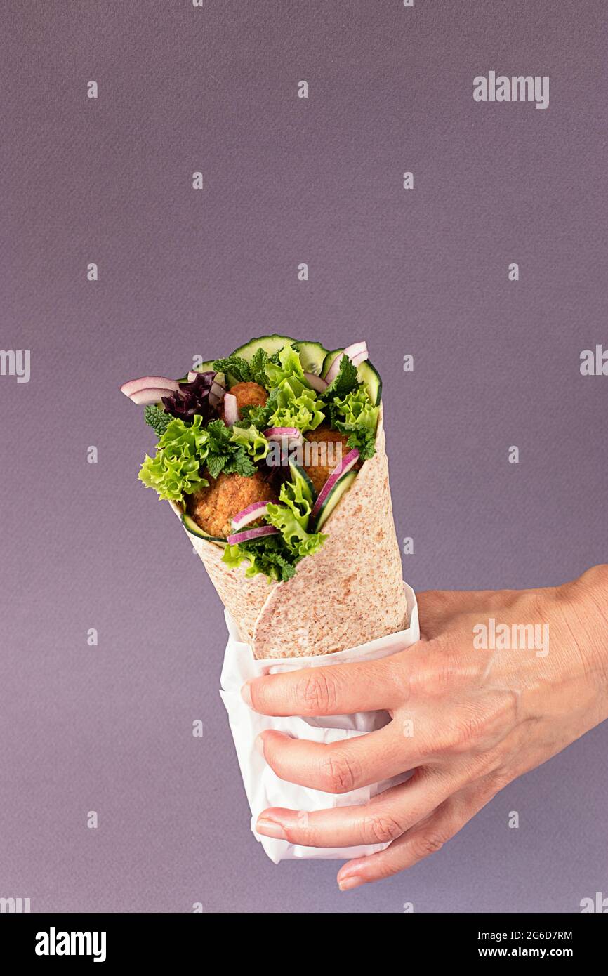 Cropped unrecognizable person hands holding vegan falafel wrap on colorful purple background Stock Photo