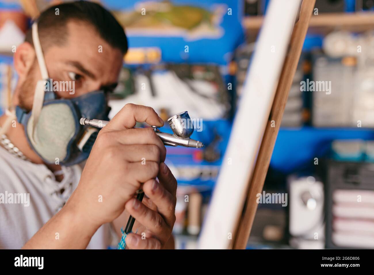 Side view of male artist in respirator using spray gun to paint picture ...