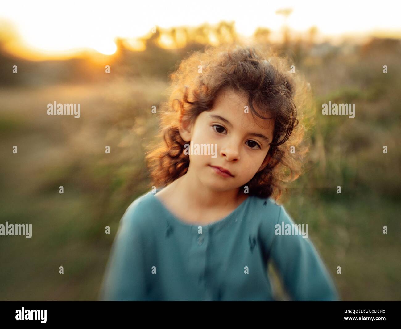 Cute little curly haired ethnic girl looking at camera against blurred