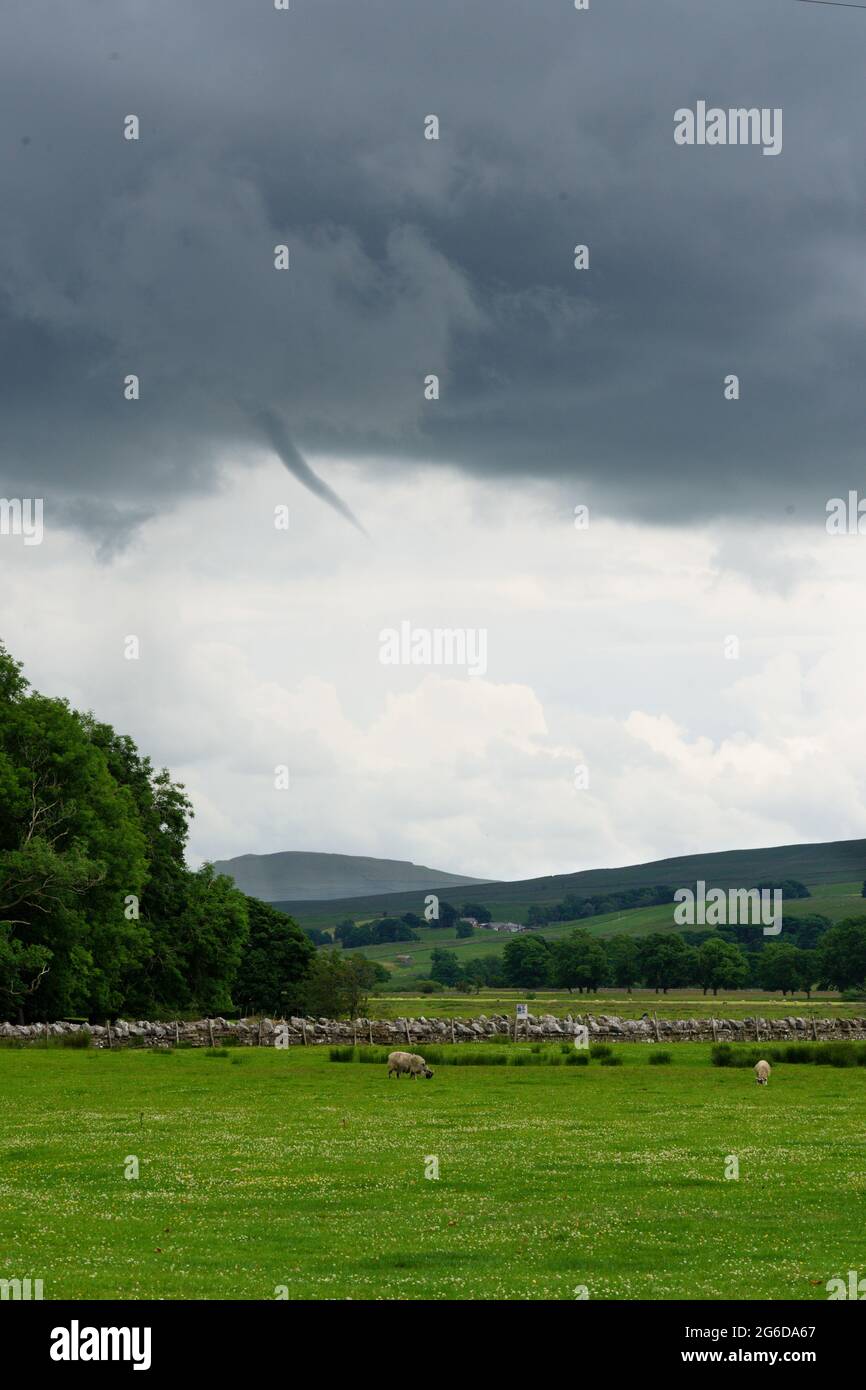 Surprising waterspout emerging from a large dark grey cloud formation above a field with Sheep grazing, Hawes, North Yorkshire, England, UK. Stock Photo