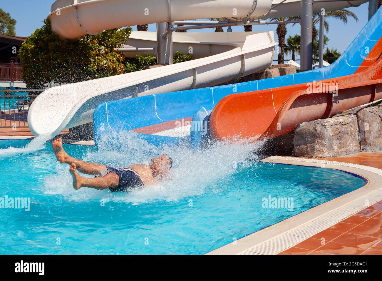 Antalya, Turkey-June 30, 2021: Man going down on water slide and entering swimming pool with big splash at aqua park in summer holiday. Stock Photo
