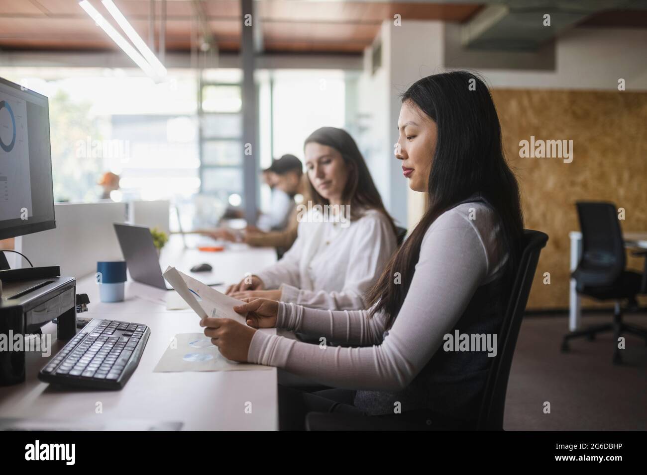 Multiracial female colleagues analyzing diagrams at table while working in modern workspace Stock Photo